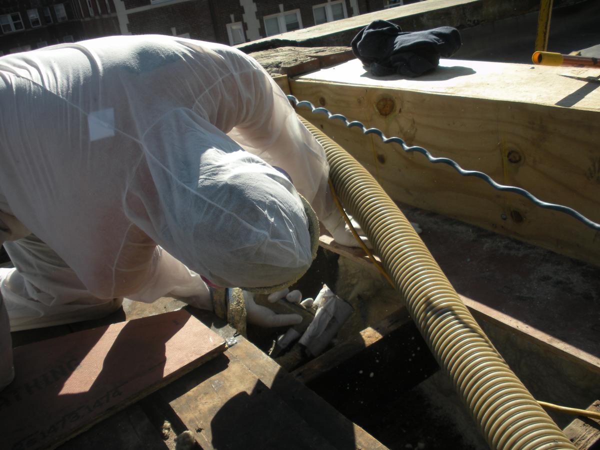 Closed-cell foam is sprayed into roof cavities along the masonry parapet wall to form a continuous air barrier between the wall and the sheathing of the flat roof.