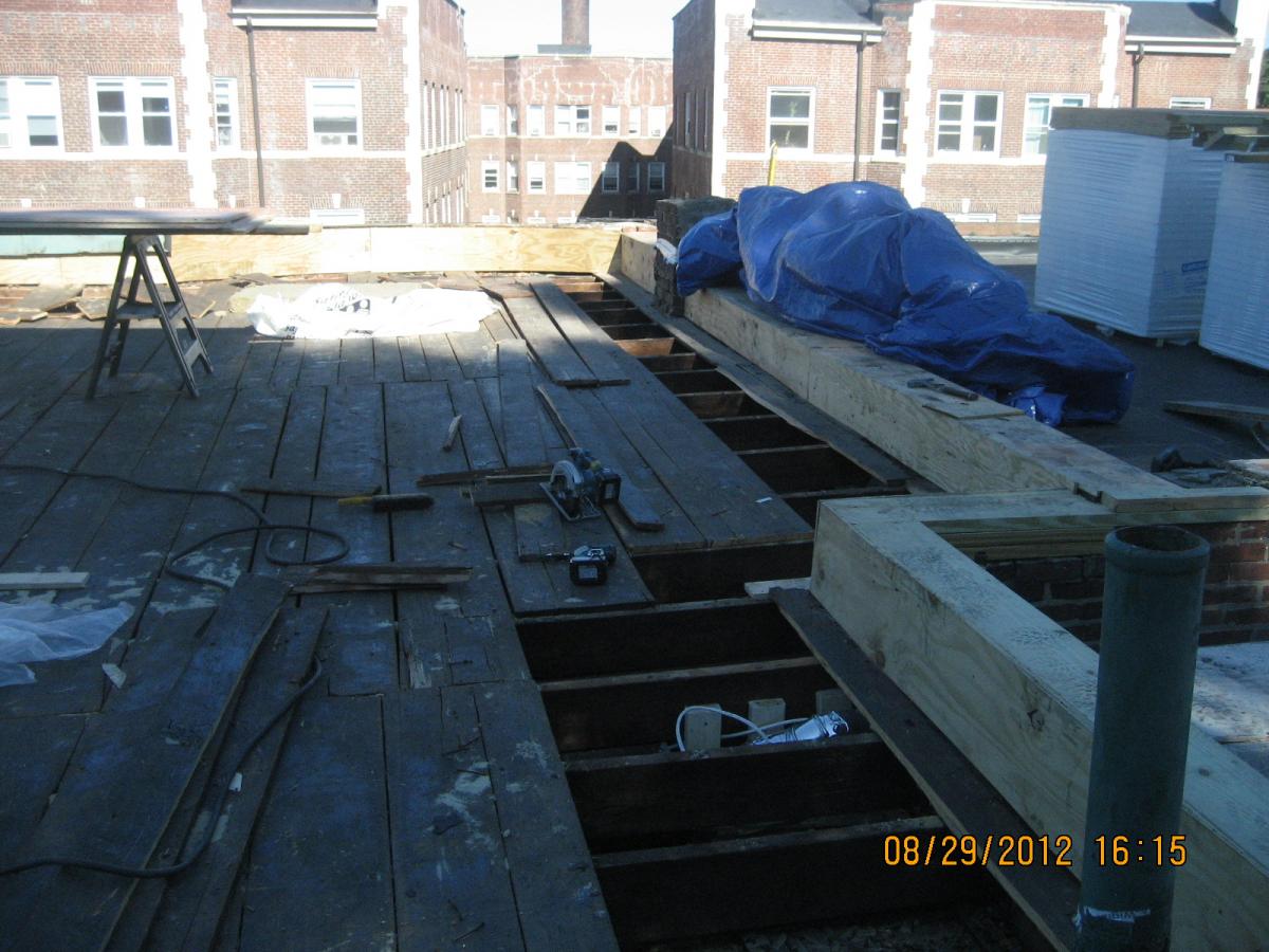 The existing sheathing boards are removed near the perimeter of the flat roof and pressure-treated plywood is installed at the vertical face of the parapet.