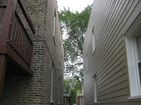 Completed wall retrofit of masonry home (on right) showing new lap siding attached over four inches of rigid foam; windows were boxed with plywood to accommodate depth of foam plus 1x4 furring strips 