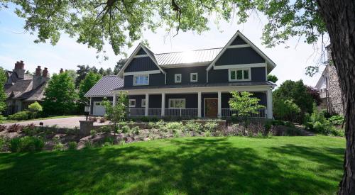 A large home with full deck at midday, framed by a front lawn and tree.