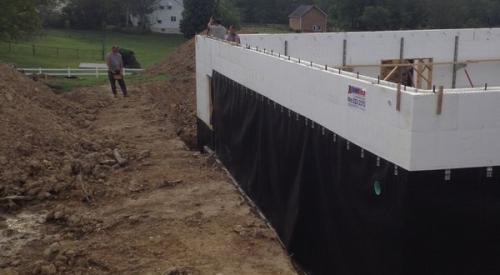 Concrete is poured into the rigid foam shell of the insulated concrete form (ICF) walls; a plastic water barrier has already been installed to protect the below-grade wall surfaces.