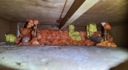 The holes around these plumbing pipes in the floor slab and in the sink cabinet have been sealed with canned spray foam to stop air leakage. 