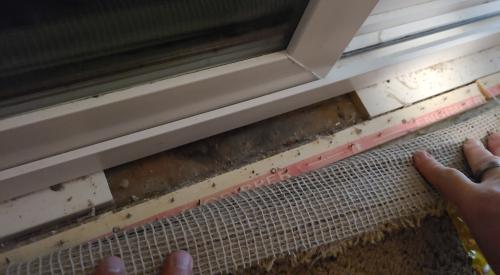 Pulling the carpet back reveals a large gap between the shims under the frame of this sliding glass door 