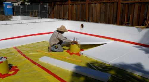 The builder laid down a 4-inch base of aggregate rock, then covered that with a plastic vapor barrier that is taped at all seams and around all penetrations before installing the rigid foam under-slab insulation.
