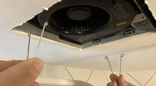 Pinch the spring-loaded mounting wires on either side of the fan to release them and remove the cover from the exhaust fan