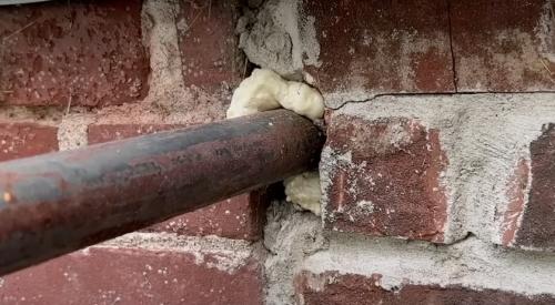 Canned spray foam is used here to seal the gap around a pipe that enters the house through the brick foundation wall 