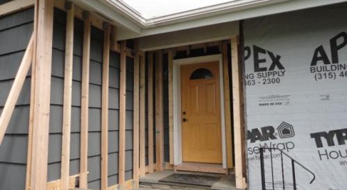 Ledger board, metal brackets, and vertical 2x4s have been installed in preparation for exterior spray foam in this retrofit exterior wall insulation technique