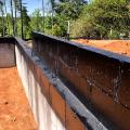 A sprayer-applied waterproofing covers the grout-filled top course of concrete foundation blocks to prevent moisture migration from the ground into the framing.