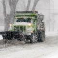 A snow plow operates along the road during a winter storm.