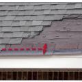 Storm-blown shingles reveal that the starter strip was incorrectly installed; rather than cutting off the tabs of the starter, the starter was rotated 180 degrees (right arrow) so the exposed portion of the first course of shingles (left arrow) was unbonded because the self-seal adhesive (dashed line) on the starter was not near the eave. 