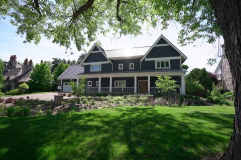 A large home with full deck at midday, framed by a front lawn and tree.