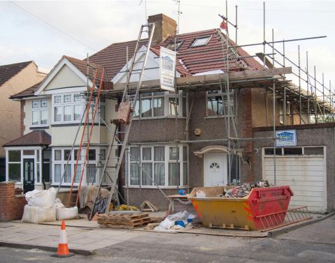 A two-story stucco home under construction; scaffolding is in place all around the exterior.