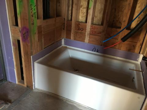 A rigid air barrier of non-paper-faced gypsum board is installed before the bathtub is installed and all seams are caulked