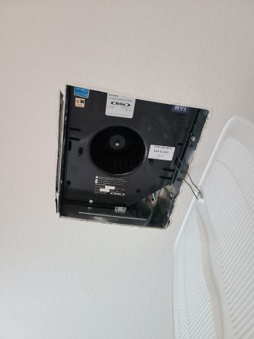 The vented cover of this bathroom exhaust fan is held in place with spring-loaded mounting wires