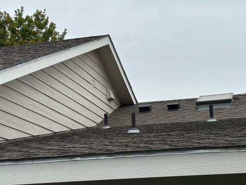 Two exhaust fan vents (with angled hoods) are visible on the roof and another exhaust vent (with angled hood) is visible on the wall of this home.