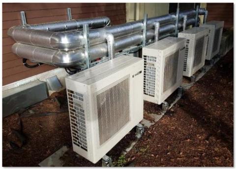 This fully specified central heat pump water heating system has four individual outdoor heat pump units plumbed in parallel to indoor storage tanks 