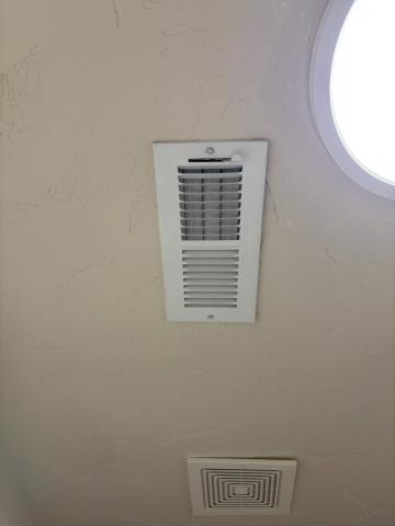 An exhaust fan (lower square grill) is installed in a laundry room ceiling next to an HVAC supply register (upper rectangular grill)