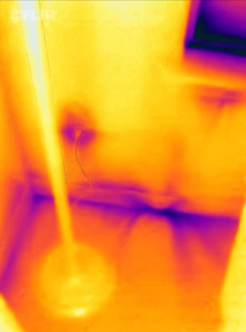 This IR camera image shows air leakage indicated by the dark purple streaks along the bottom plates and below the window sill, as well as some heat loss at the electric outlet. 