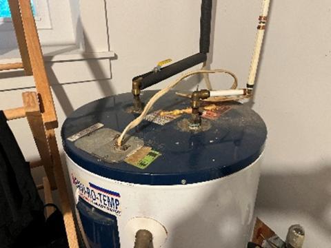 The inlet and outlet water pipe connections are located on top of this electric water heater; note that the hot water line (on the left) has been insulated.