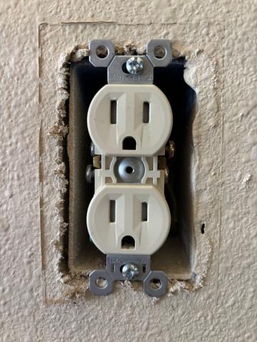 The cover plate has been removed from this outlet, exposing the gap between the electrical box and the drywall.