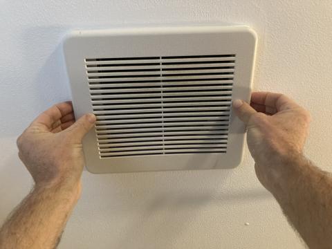Pull the exhaust fan vent cover down gently to access the spring-loaded mounting wires