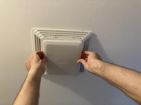 Press in on the sides of the plastic light cover to remove the light cover from the bathroom exhaust fan for cleaning
