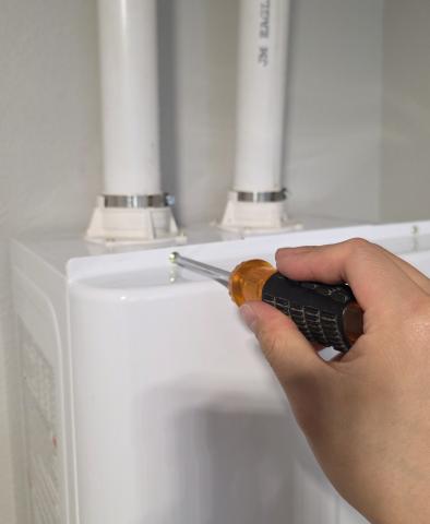 Use a screwdriver to remove the front panel of a tankless water heater to access the air filter or other internal components