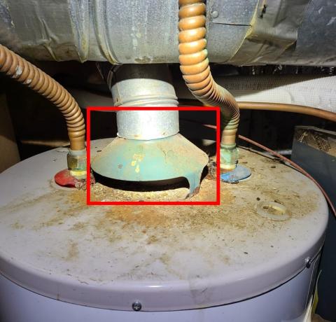 This ambient-drafted gas water heater has backdrafted in the past or is actively backdrafting, as indicated by the melted plastic rings around the gas pipe and soot spots on the top of the tank; backdrafting brings dangerous carbon monoxide into the home.