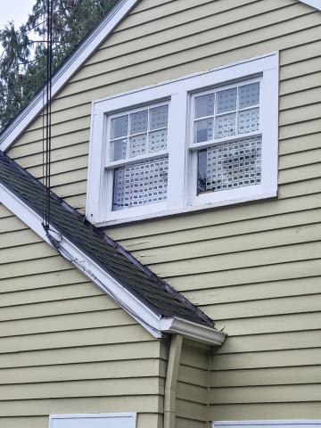 This step flashing was installed over, not under, the siding, so water is getting behind the step flashing and rotting the siding; the house was also badly designed with a window frame that touches the intersecting roof, inviting interior water damage.