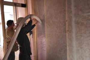 After attaching netting to the 2x6 studs, workers fill the wall cavities with R-23 of blown fiberglass made from recycled bottles.