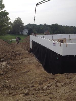 Concrete is poured into the rigid foam shell of the insulated concrete form (ICF) walls; a plastic water barrier has already been installed to protect the below-grade wall surfaces.