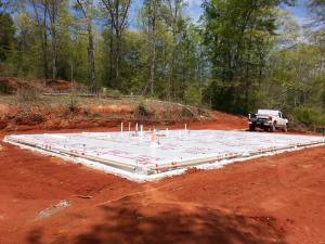 To help keep the monolithic slab-on-grade foundation dry, the site’s surfaces is graded away from the structure, the slab is poured on a bed of gravel, and using a vapor barrier will separate the foundation from the sill plates. 
