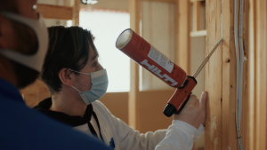 Right – A student uses a powered caulk gun to air seal wood-to-wood seams.
