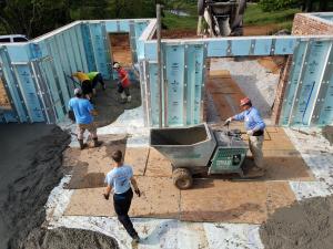 Right – Workers pour the concrete for the basement floor slab over a vapor barrier installed over rigid foam.