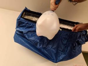 A foaming cleaner is used to clean the coils inside this ductless indoor unit; a mini-split bib surrounds the unit to contain overspray and drips