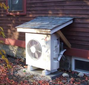 This simple awning keeps rain, snow, and leaves from collecting on the HVAC unit; however, the awning should be higher above the heat pump and there should be metal L flashing and a gap separating the wood siding from the roofing material.