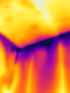 The dark purple areas and long streaks in this IR camera image show extreme cold spots along the top of the walls, indicating a lack of both air sealing and insulation above the top plates of these walls. 