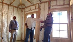 A builder, energy efficiency consultant, and crew supervisor inspect a spray foam installation. 