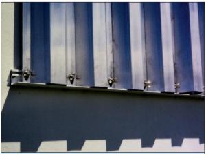 Right – This metal panel window shutter is installed in a track permanently mounted above and below the window frame and is secured with wing nuts to studs mounted on the track. 