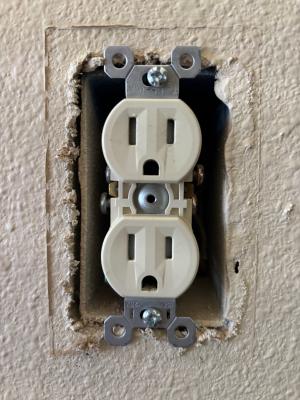 The cover plate has been removed from this outlet, exposing the gap between the electrical box and the drywall.