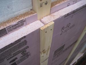 This close-up of an exterior wall retrofit of a masonry brick home shows the fluid-applied water and air control layer (white), 2x4 furring strips and two layers of rigid foam insulation (pink), then 1x4 furring which provides a ventilation gap