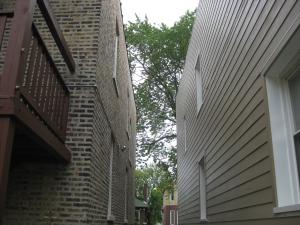 Completed wall retrofit of masonry home (on right) showing new lap siding attached over four inches of rigid foam; windows were boxed with plywood to accommodate depth of foam plus 1x4 furring strips 