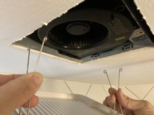Pinch the spring-loaded mounting wires on either side of the fan to release them and remove the cover from the exhaust fan