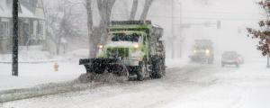 A snow plow operates along the road during a winter storm.
