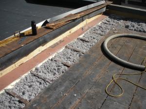 Roofing paper protects the top of the new plywood parapet while the base of the parapet is air sealed with spray foam and fibrous insulation is installed in the rafter cavities in this flat roof retrofit