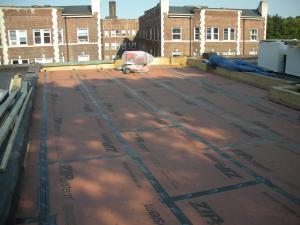 New coated OSB roof sheathing is installed over the existing sheathing of the flat roof and taped at the seams to provide a continuous air barrier