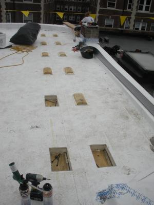 Roofing membrane is installed over polyisocyanurate rigid foam insulation and insulation cover board that has been cut to fit around locations for blocking for the PV system rack