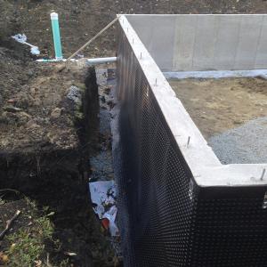A dimpled rain mat and perforated drain pipe provide drainage around the basement foundation.