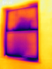 The dark purple patches at the sill and streaks at the meeting rail of the window in this IR camera image indicate heat loss and significant air leakage.