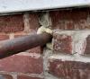 Canned spray foam is used here to seal the gap around a pipe that enters the house through the brick foundation wall 
